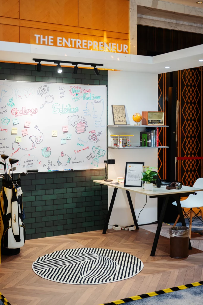 Interactive office-themed display booth titled The Entrepreneur with a whiteboard desk setup and golf bag